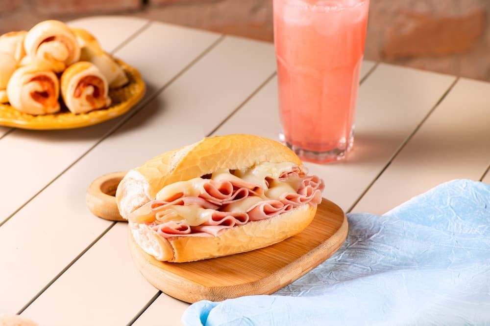 Sanduíche de mortadela com queijo no pão francês, com suco.