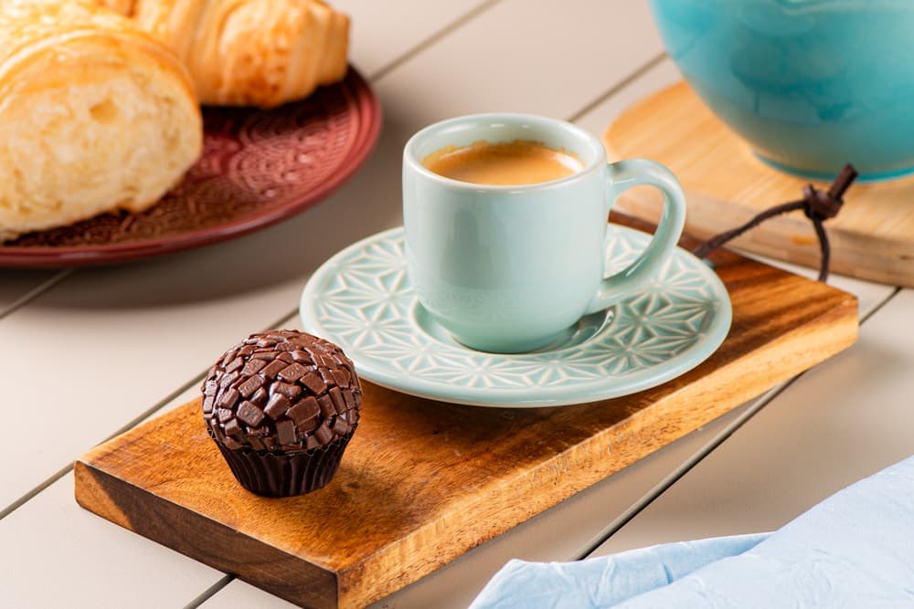 Café expresso em xícara verde com brigadeiro ao lado.