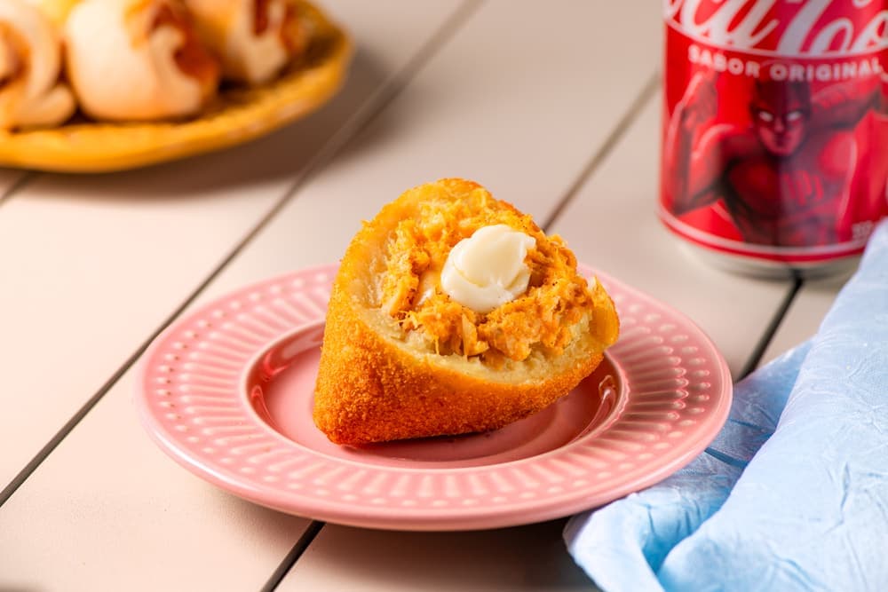 Coxinha aberta em prato rosa, com refrigerante.