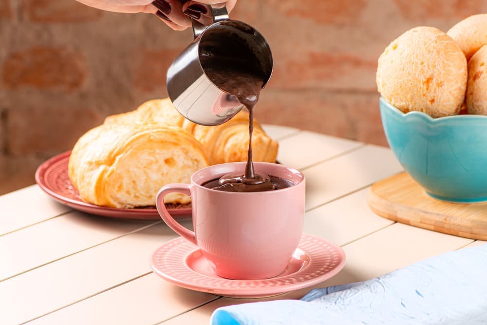Café sendo servido na xícara rosa, com croissant e pão de queijo.
