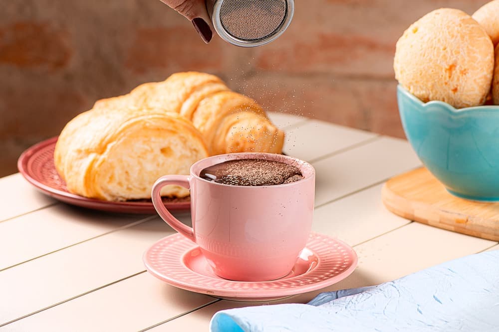 Café sendo servido na xícara rosa, com croissant e pão de queijo.