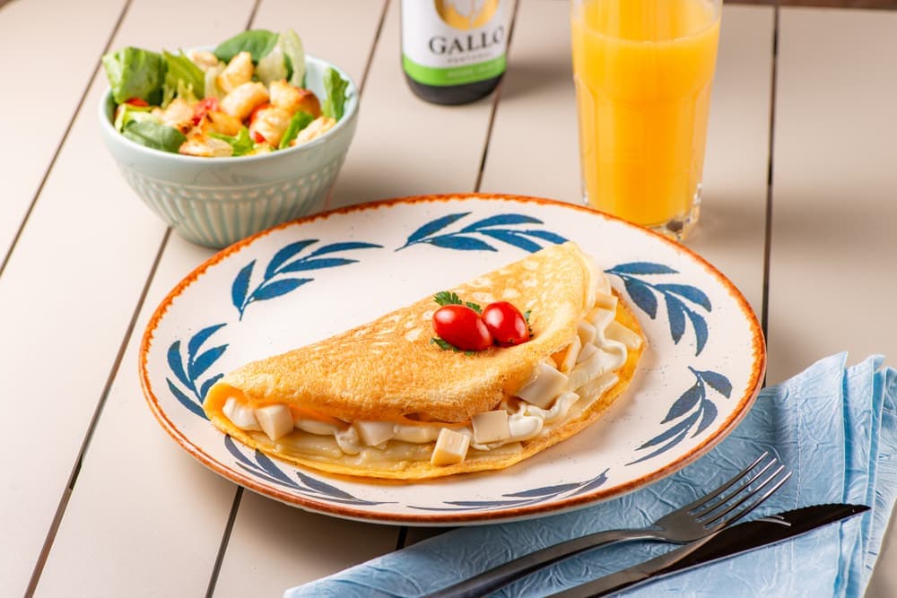 Omelete em prato azul, com salada e suco de laranja.