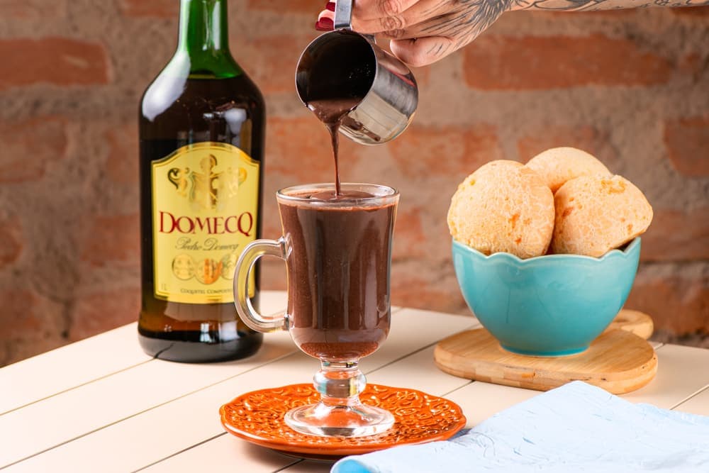 Chocolate quente com licor em taça, com pães de queijo.