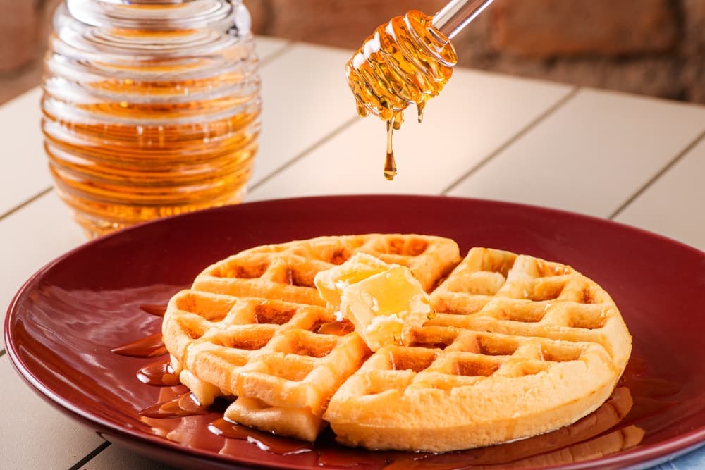 Waffle com manteiga e mel em prato vermelho.