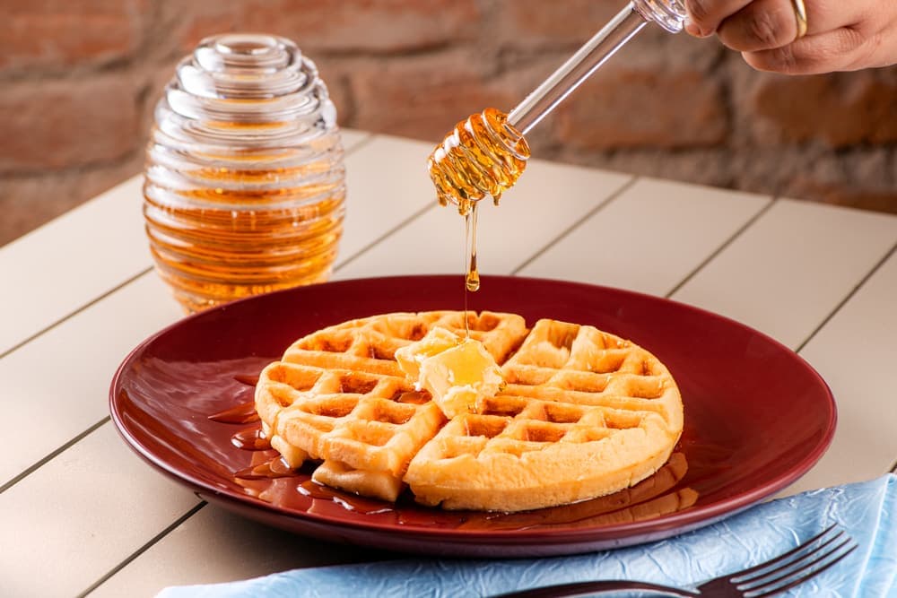 Waffle com mel sendo servido, em prato vermelho.