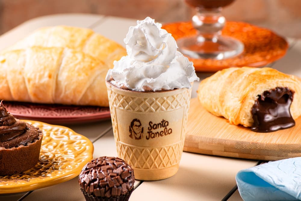 Chocolate quente com chantilly no copo Santa Janela, com croissants.