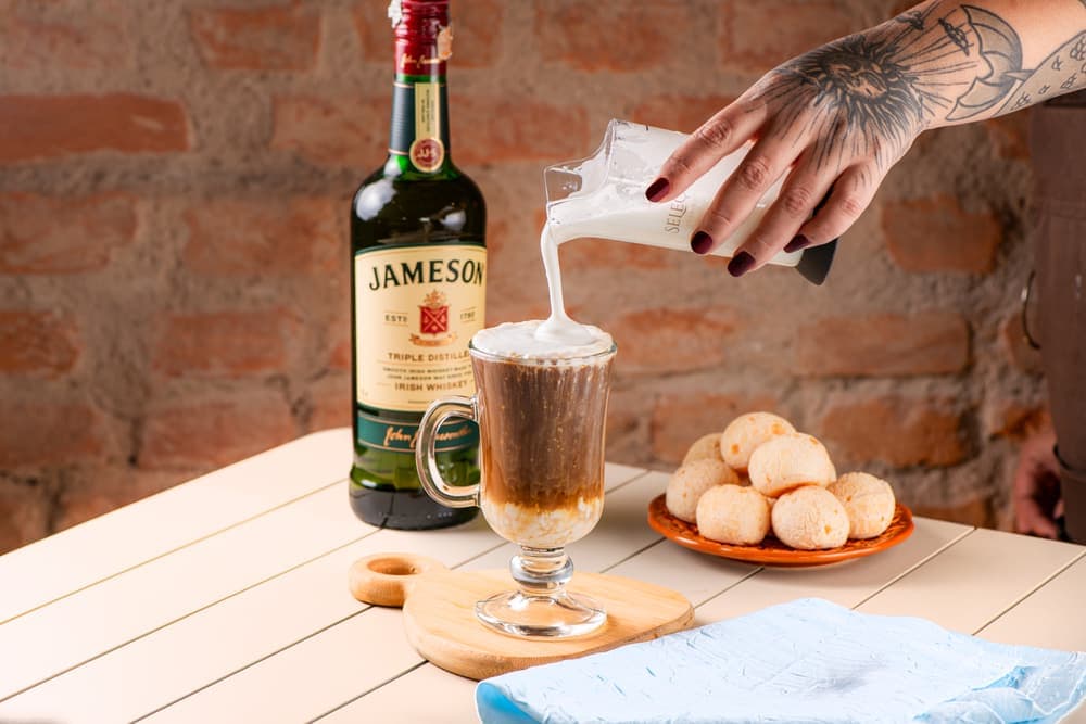 Café com licor sendo servido em taça, com pães de queijo.