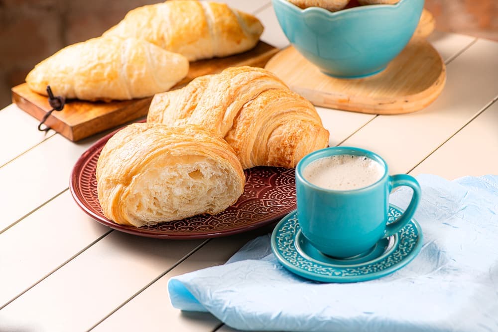 Croissant folhado com café com leite em xícara azul.