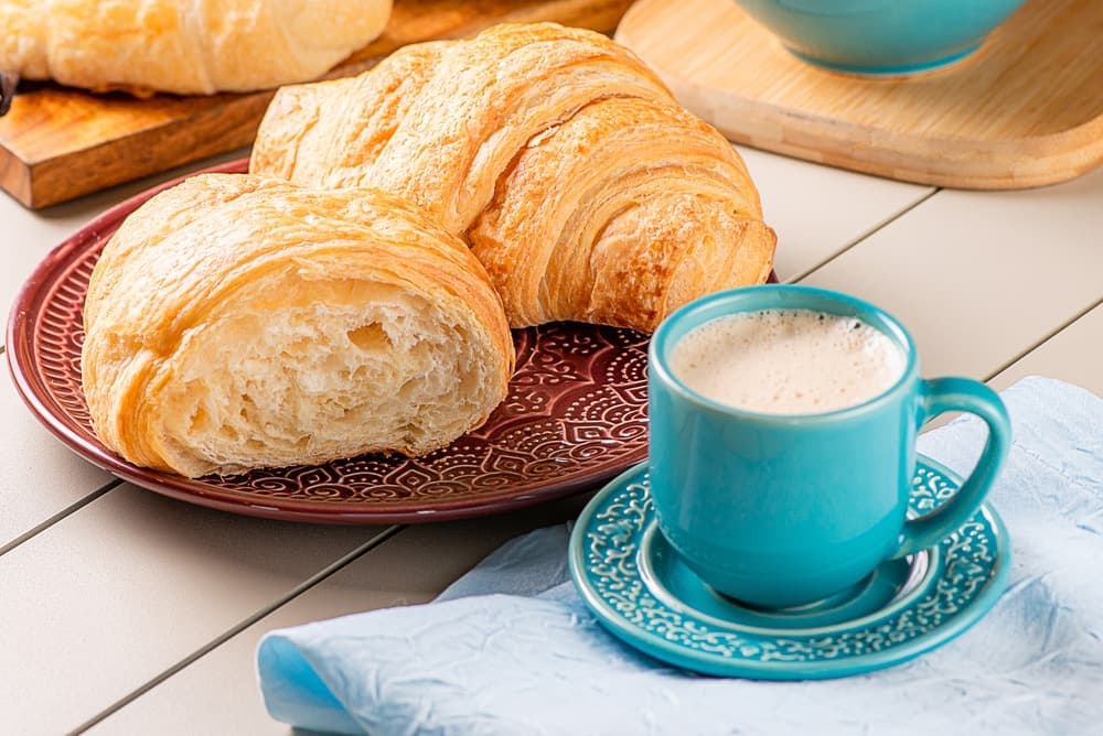 Croissant folhado com café com leite em xícara azul.