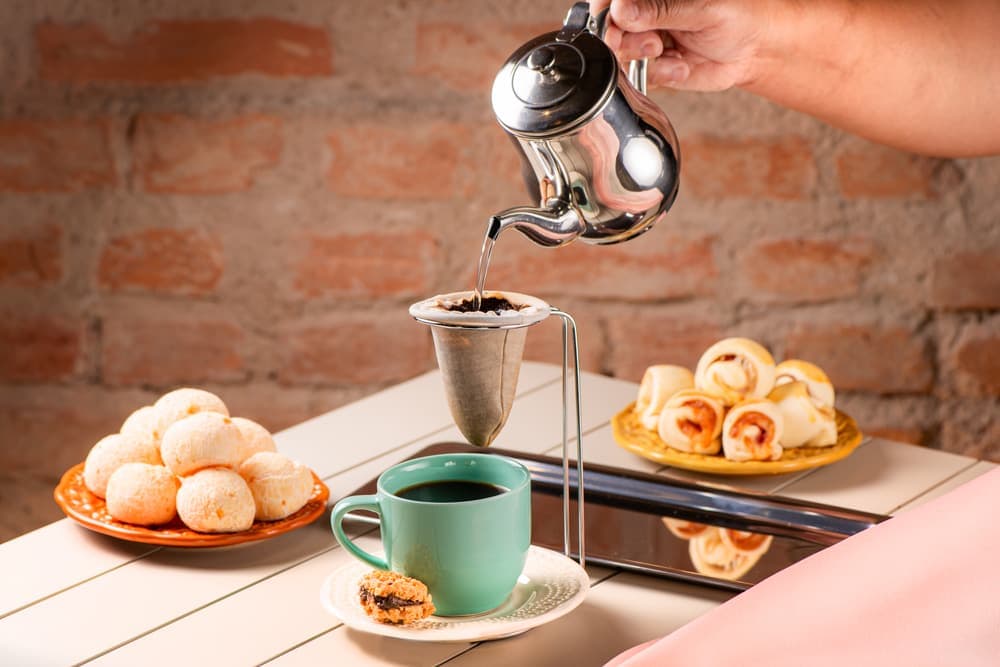 Café sendo servido na xícara verde, com enroladinhos.